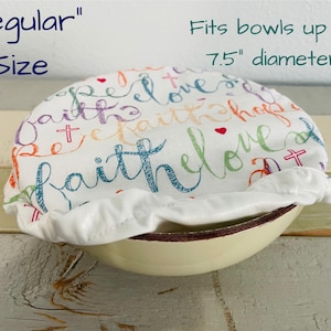 Reusable "Regular Sized" bowl covers in "Faith Hope Love" print": a white fabric bowl cover with the words "faith", "hope", and "love" in colorful script. The cover fits bowls up to 7.5 inches in diameter.