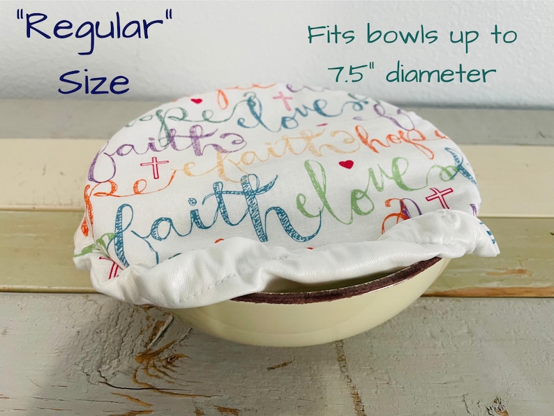Reusable "Regular Sized" bowl covers in "Faith Hope Love" print": a white fabric bowl cover with the words "faith", "hope", and "love" in colorful script. The cover fits bowls up to 7.5 inches in diameter.