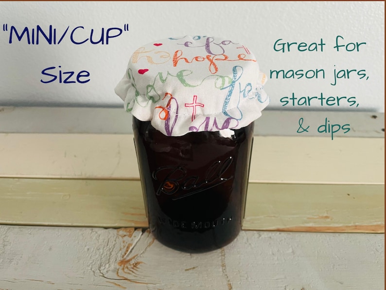 A glass mason jar with a fabric lid featuring "Faith Hope Love" print - a colorful script and a cross design. The jar is labeled "MINI/CUP" and "Size". The text "Great for mason jars, starters, & dips" is also visible.