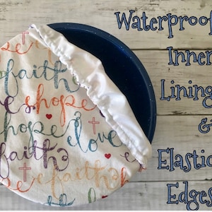 Reusable bowl cover in "Faith Hope Love" print: white fabric with elastic edges, featuring the words "faith, hope, love" in colorful script, along with cross and heart symbols. The cover is shown over a blue bowl, with text that reads "Waterproof Inner Lining & Elastic Edges."