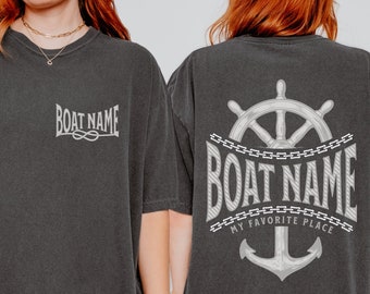 May include: A black t-shirt with a white anchor and steering wheel graphic. The text "BOAT NAME MY FAVORITE PLACE" is printed on the shirt.