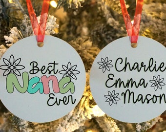 May include: Two round white ornaments with red ribbon hangers. One ornament says "Best Nana Ever" with a green, blue, and pink design. The other ornament says "Charlie Emma Mason" with a black and white flower design.