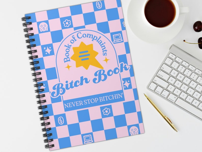 May include: A pink and blue chequered notebook with the text "Book of Complaints Bitch Book NEVER STOP BITCHIN'" in a retro font. The notebook has a spiral binding and a yellow speech bubble with three lines.