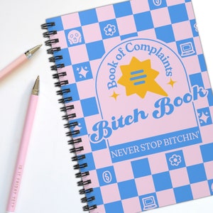 May include: A pink and blue checkered notebook with a spiral binding. The cover features the text "Book of Complaints Bitch Book" in a retro font with a yellow speech bubble and stars. The text "NEVER STOP BITCHIN'" is printed below the title.