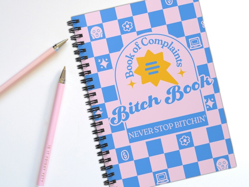 May include: A pink and blue checkered notebook with a spiral binding. The cover features the text "Book of Complaints Bitch Book" in a retro font with a yellow speech bubble and stars. The text "NEVER STOP BITCHIN'" is printed below the title.