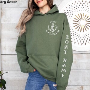 May include: A military green hooded sweatshirt with the text "DROP SOME ANCHOR" and an anchor graphic on the front. The left sleeve has the text "BOAT NAME" printed vertically.