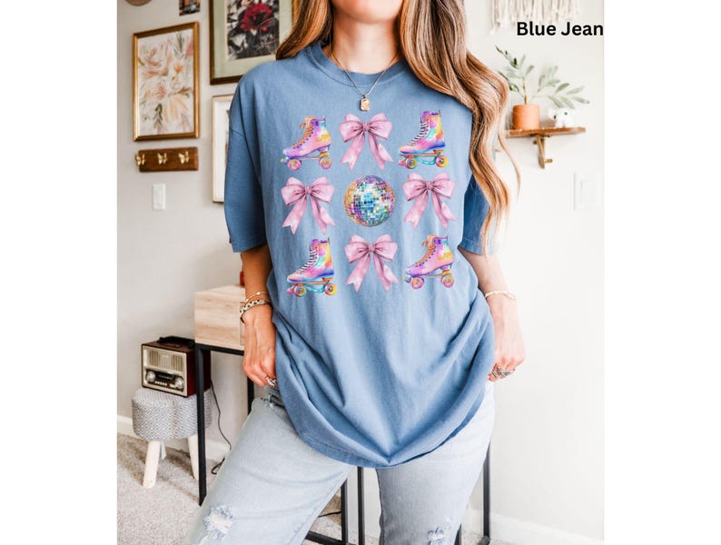 May include: A blue jean t-shirt featuring a graphic print of pink bows and roller skates with disco balls. The text "Blue Jean" is visible in the top right corner of the image.