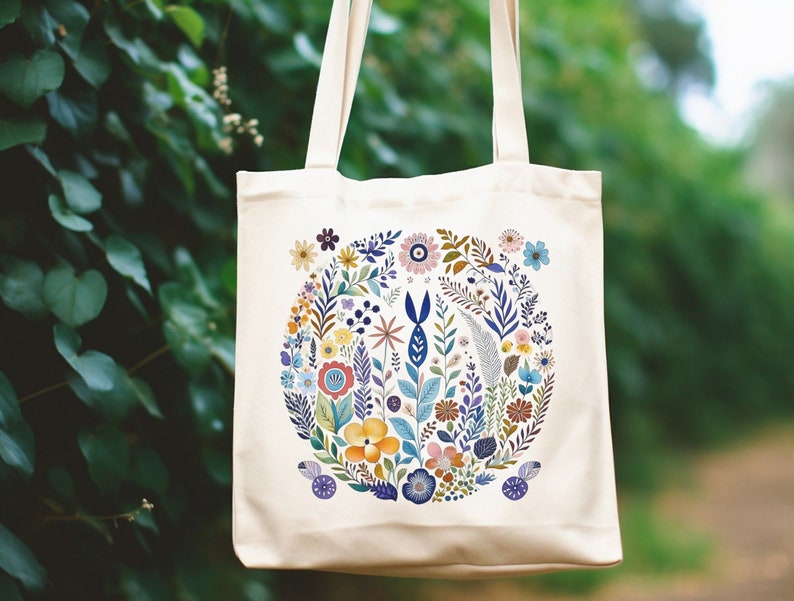May include: A white canvas tote bag with a colorful floral design. The flowers are arranged in a circle and include blue, pink, yellow, and green colors.