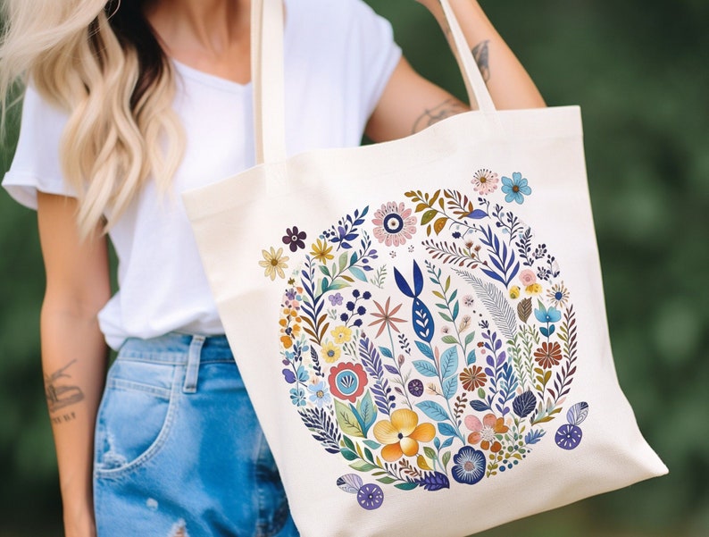 May include: A white canvas tote bag with a colorful floral design. The design features a variety of flowers, leaves, and stems in shades of blue, yellow, pink, and green.