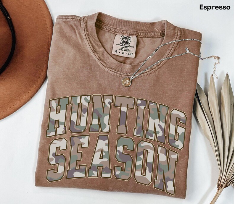 K&ouml;nnte beinhalten: Ein braunes T-Shirt mit einem Tarnmuster, auf dem "Hunting Season" steht.