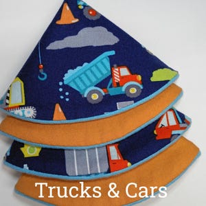 May include: A stack of three fabric pieces with a dark blue background featuring a construction vehicle print, including dump trucks, cranes, and orange traffic cones. Each piece has a solid mustard yellow underside and light blue piping.