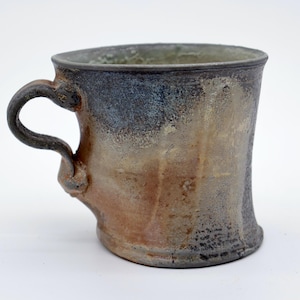 May include: A handmade ceramic mug with a unique, textured surface. The mug features a curved handle and a color palette of brown, blue, and beige. The mug's design is rustic and organic, suitable for coffee or tea.