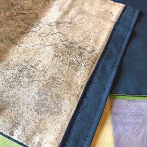 Può includere: Un tessuto beige con un motivo maculato grigio scuro. Il tessuto è cucito a un bordo in tessuto nero.