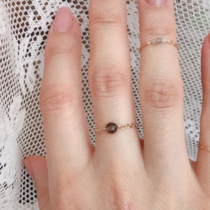 May include: A hand wearing four delicate gold rings with small gemstones. The rings are on the index, middle, ring, and little fingers. The nails are painted a light nude colour.