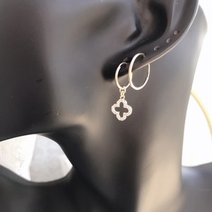 May include: Gold hoop earrings with a dangling clover charm set with clear cubic zirconia stones.
