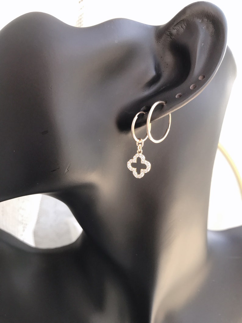 May include: Gold hoop earrings with a dangling clover charm set with clear cubic zirconia stones.