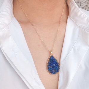 May include: A gold chain necklace with a teardrop-shaped pendant made of wire and blue beads.