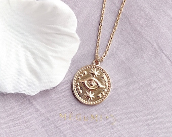 May include: Gold necklace with a round pendant featuring a stylised eye with stars around it.