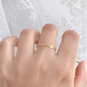 May include: A delicate gold chain ring with oval links. The ring is worn on a finger.