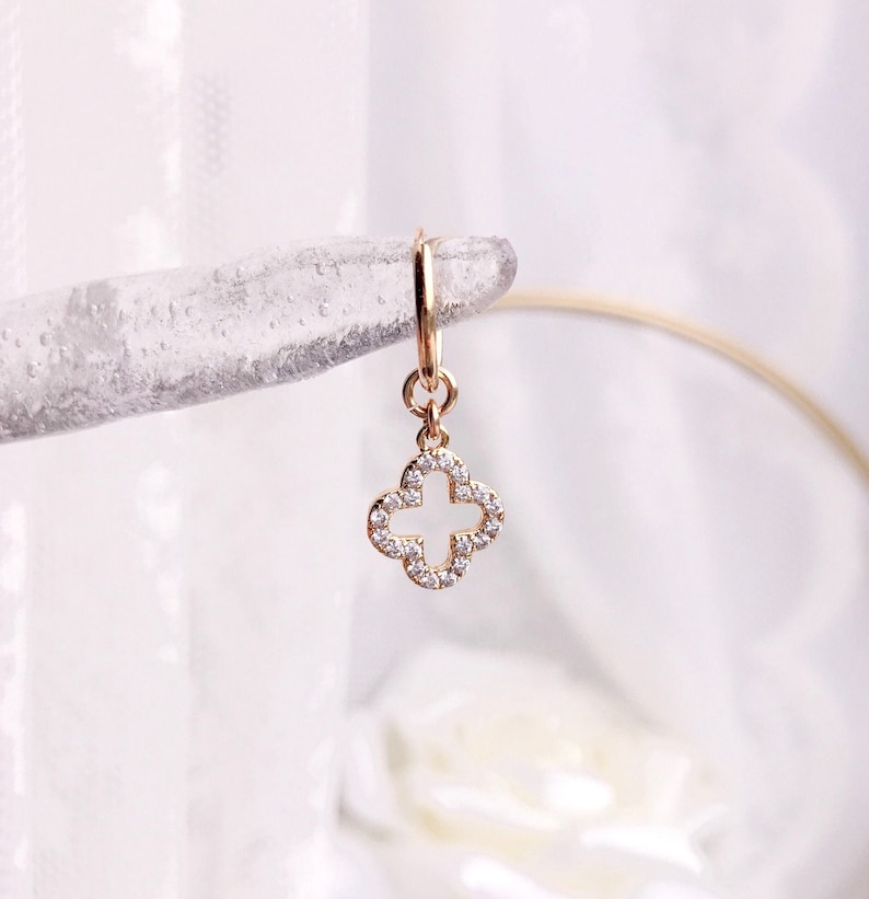 May include: Gold hoop earring with a dangling four-leaf clover charm. The clover is encrusted with small clear rhinestones.