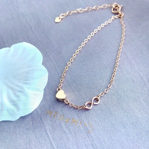 May include: A delicate gold chain bracelet with a heart charm and an infinity symbol charm.