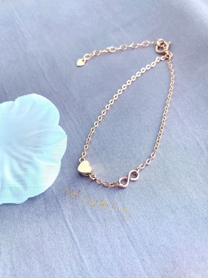 May include: A delicate gold chain bracelet with a heart charm and an infinity symbol charm.