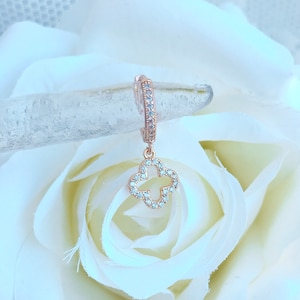 Puede incluir: Aretes de aro de oro rosa con un dije de tr&eacute;bol de cuatro hojas colgante, ambos adornados con piedras de circonita c&uacute;bica transparentes.
