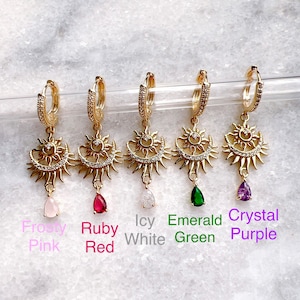 Puede incluir: Cinco pendientes de aro de oro con un dije de sol y luna y una piedra preciosa colgante. Las piedras preciosas son rosa helado, rojo rubí, blanco helado, verde esmeralda y morado cristal.