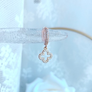 Puede incluir: Aretes de aro de oro rosa con un dije colgante de tr&eacute;bol de cuatro hojas. El tr&eacute;bol est&aacute; incrustado con piedras de circonita c&uacute;bica transparentes.