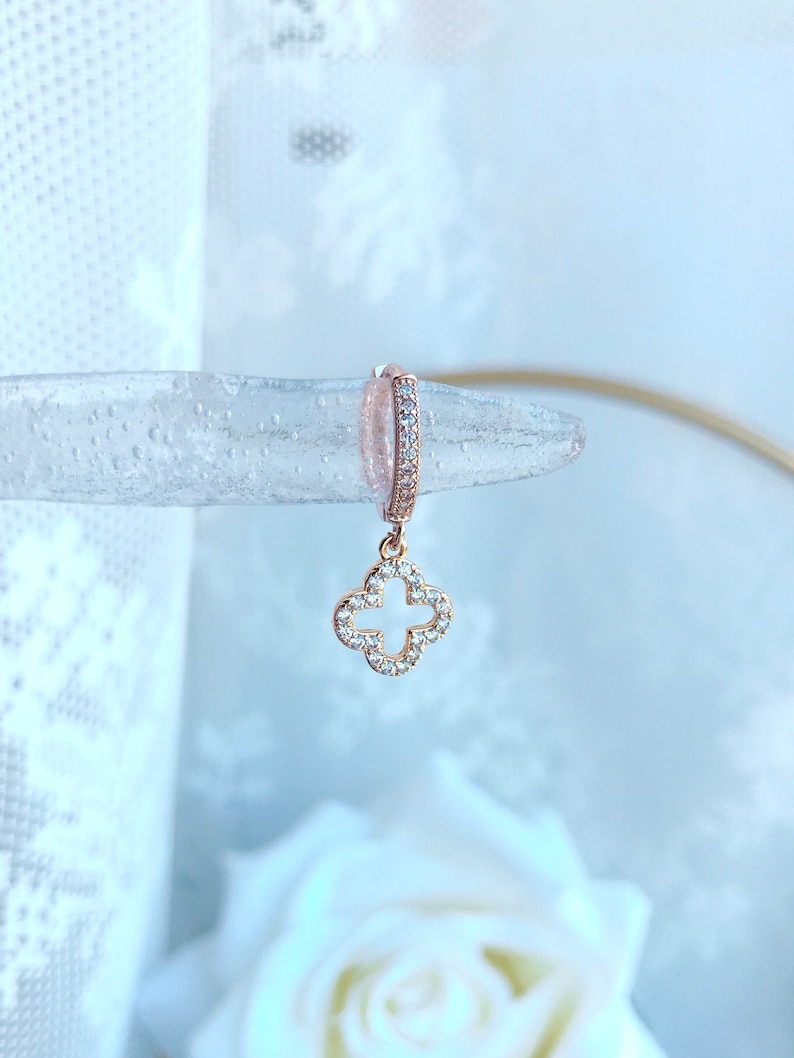 Puede incluir: Aretes de aro de oro rosa con un dije colgante de tr&eacute;bol de cuatro hojas. El tr&eacute;bol est&aacute; incrustado con piedras de circonita c&uacute;bica transparentes.