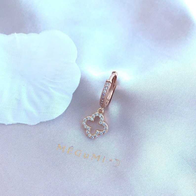 Puede incluir: Aretes de aro de oro rosa con un dije de tr&eacute;bol colgante. El tr&eacute;bol est&aacute; incrustado con piedras de circonita c&uacute;bica transparentes.