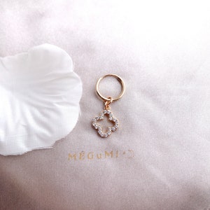 May include: Gold hoop earrings with a dangling charm in the shape of a four-leaf clover, adorned with clear cubic zirconia stones.