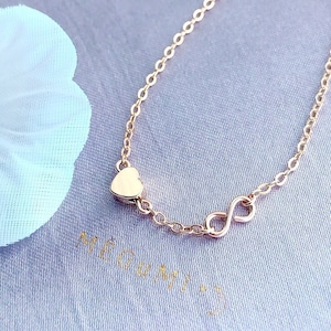 Puede incluir: Un delicado collar de cadena dorada con un pequeño dije de corazón y un dije de símbolo de infinito.