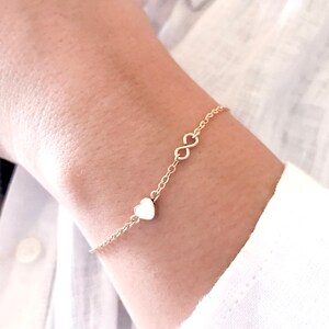 May include: A gold chain bracelet with a small heart charm and an infinity symbol charm.
