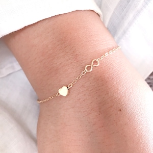 May include: A gold chain bracelet with a small heart charm and an infinity symbol charm.