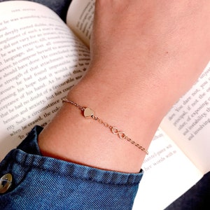 May include: A gold chain bracelet with a heart and infinity symbol charms. The bracelet is on a person's wrist.