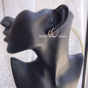 May include: Two silver hoop earrings, one 12mm and one 16mm in diameter, shown on a black mannequin head.