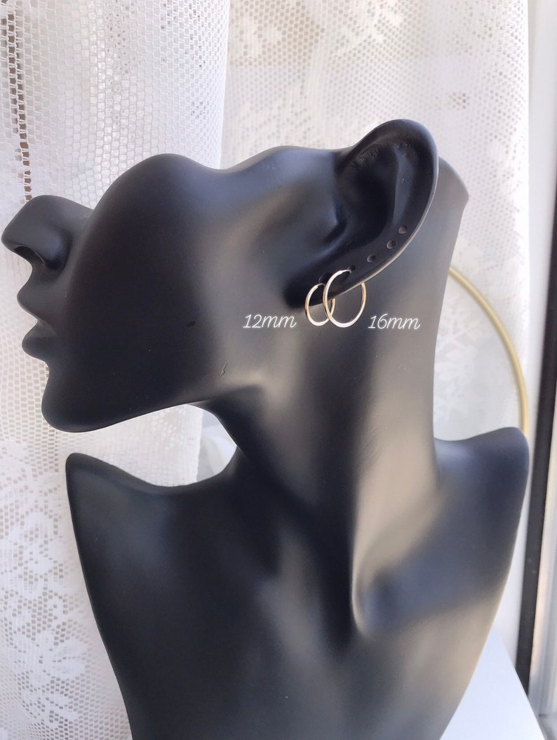 May include: Two silver hoop earrings, one 12mm and one 16mm in diameter, shown on a black mannequin head.
