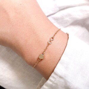 May include: A gold chain bracelet with a heart charm and an infinity symbol charm.