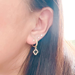 Puede incluir: Aretes de aro dorados con un dije colgante de tr&eacute;bol de cuatro hojas. El tr&eacute;bol est&aacute; incrustado con peque&ntilde;as piedras transparentes.