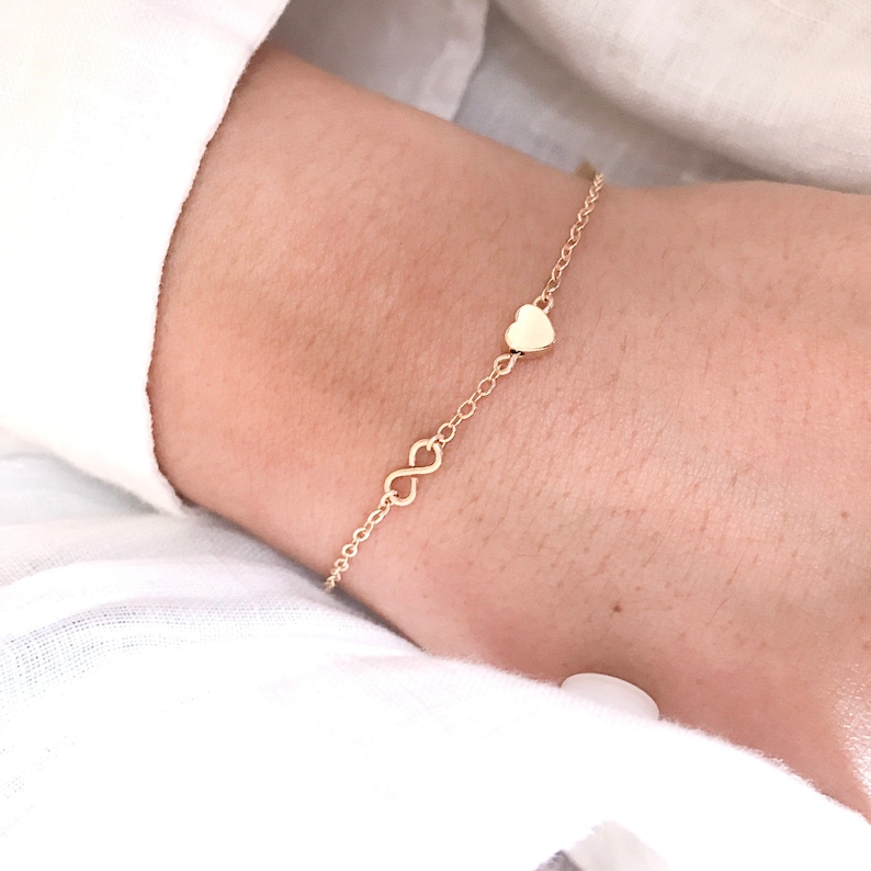 May include: A gold chain bracelet with an infinity symbol and a small heart charm.