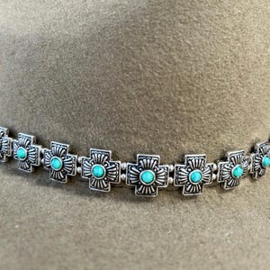 May include: A silver hat band with turquoise stones in the shape of crosses.