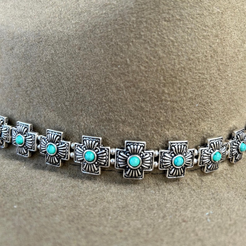 May include: A silver hat band with turquoise stones in the shape of crosses.
