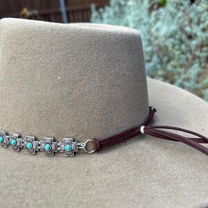 May include: A brown felt cowboy hat with a brown leather hatband and turquoise and silver embellishments.