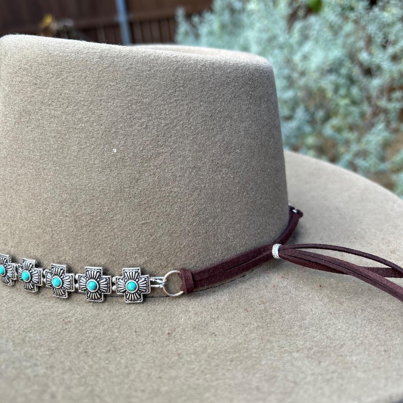 May include: A brown felt cowboy hat with a brown leather hatband and turquoise and silver embellishments.