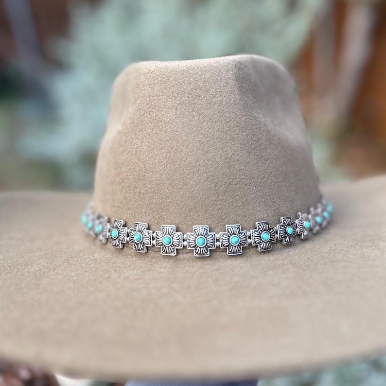 May include: A brown felt fedora hat with a silver and turquoise cross-shaped band.