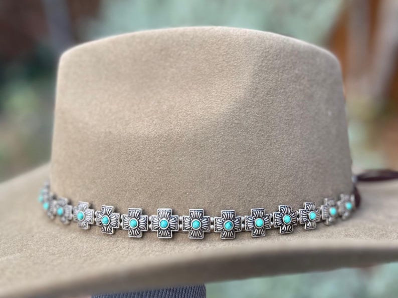 May include: A tan felt cowboy hat with a silver and turquoise hat band. The hat band is made of a repeating pattern of silver crosses with turquoise stones in the center.