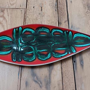 Puede incluir: Una fuente de cerámica larga y ovalada con una base roja vibrante. La fuente presenta un diseño central de formas abstractas en verde azulado, negro y naranja. Los bordes están delineados en blanco, creando un contraste llamativo. Ideal para aperitivos.