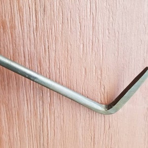May include: A close-up of a metal pry bar with a curved end. The bar is silver in color and has a slightly textured surface.