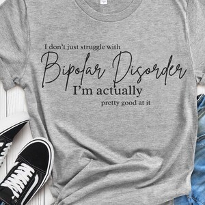 May include: Gray t-shirt with black text that reads "I don't just struggle with Bipolar Disorder I'm actually pretty good at it."